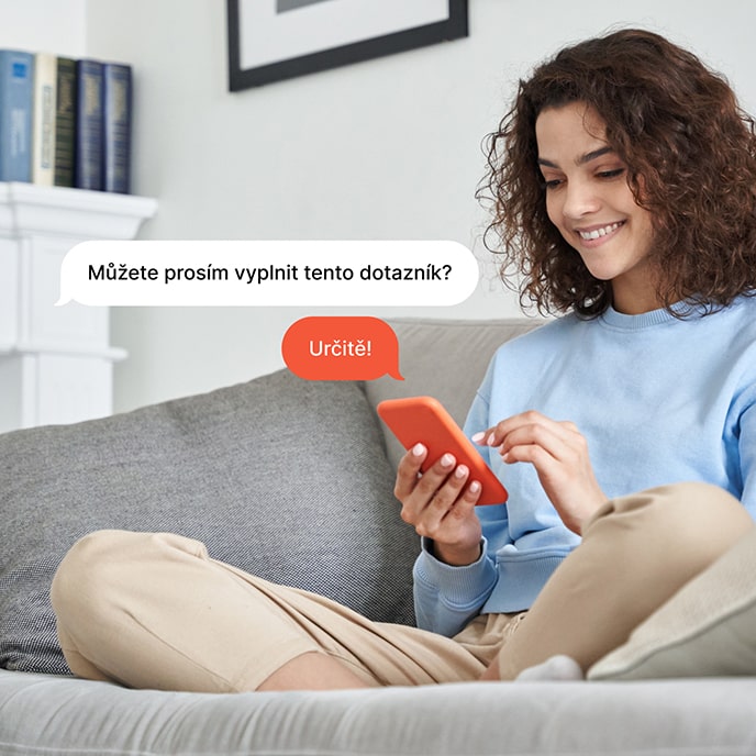 Žena sedící na pohovce vyplňuje dotazník v mobilním telefonu